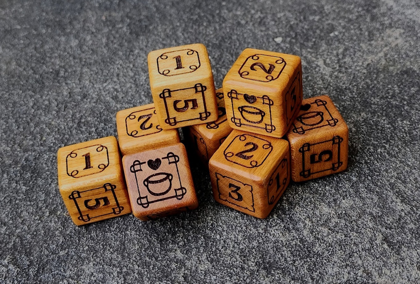 A stack of six brown, wooden d6 dice, each engraved with a custom face. Numbers 1-5 have numerals, the 6 face has a stewpot with a heart over it.