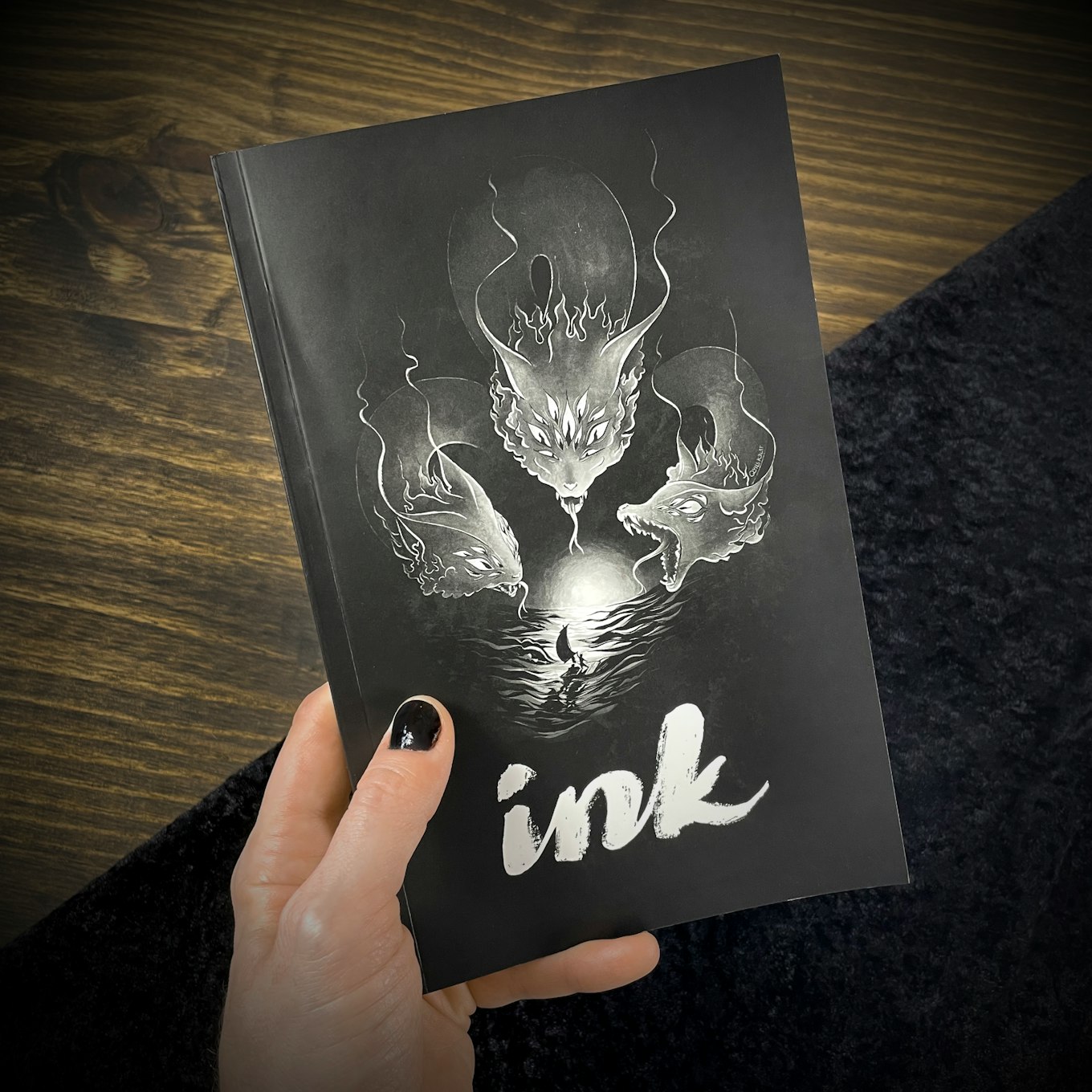 A hand holding a copy of the ink softcover book